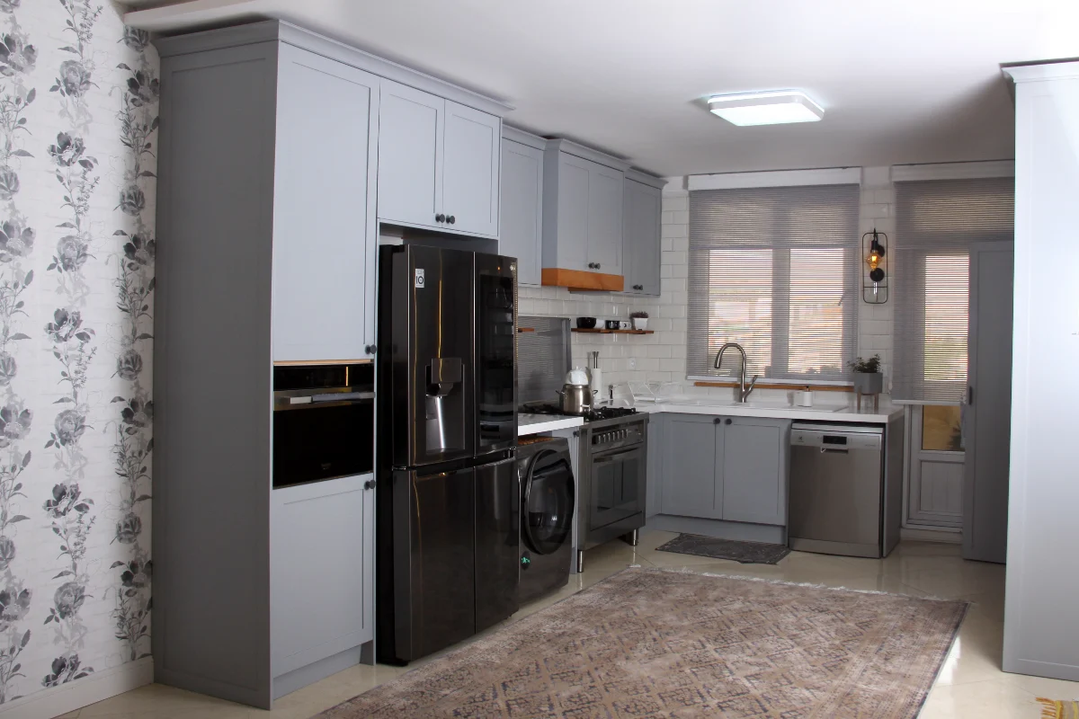 آشپزخانه با کابینت‌های طوسی روشن و گاز و ماشین ظرفشویی و لباسشویی استیل