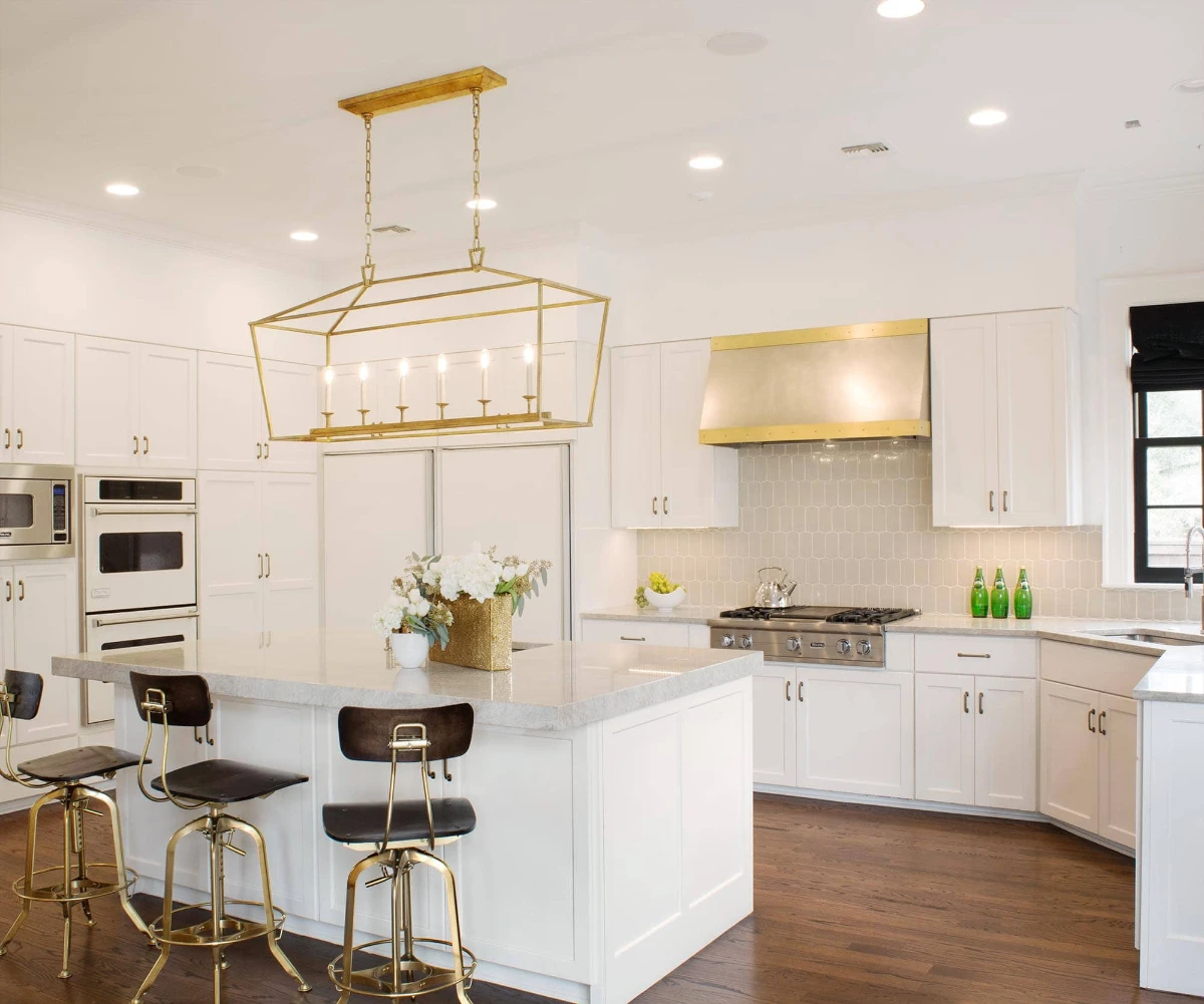 کابینت سفید آشپزخانه نئوکلاسیک با کاور هود و لوستر و صندلی‌های طلایی